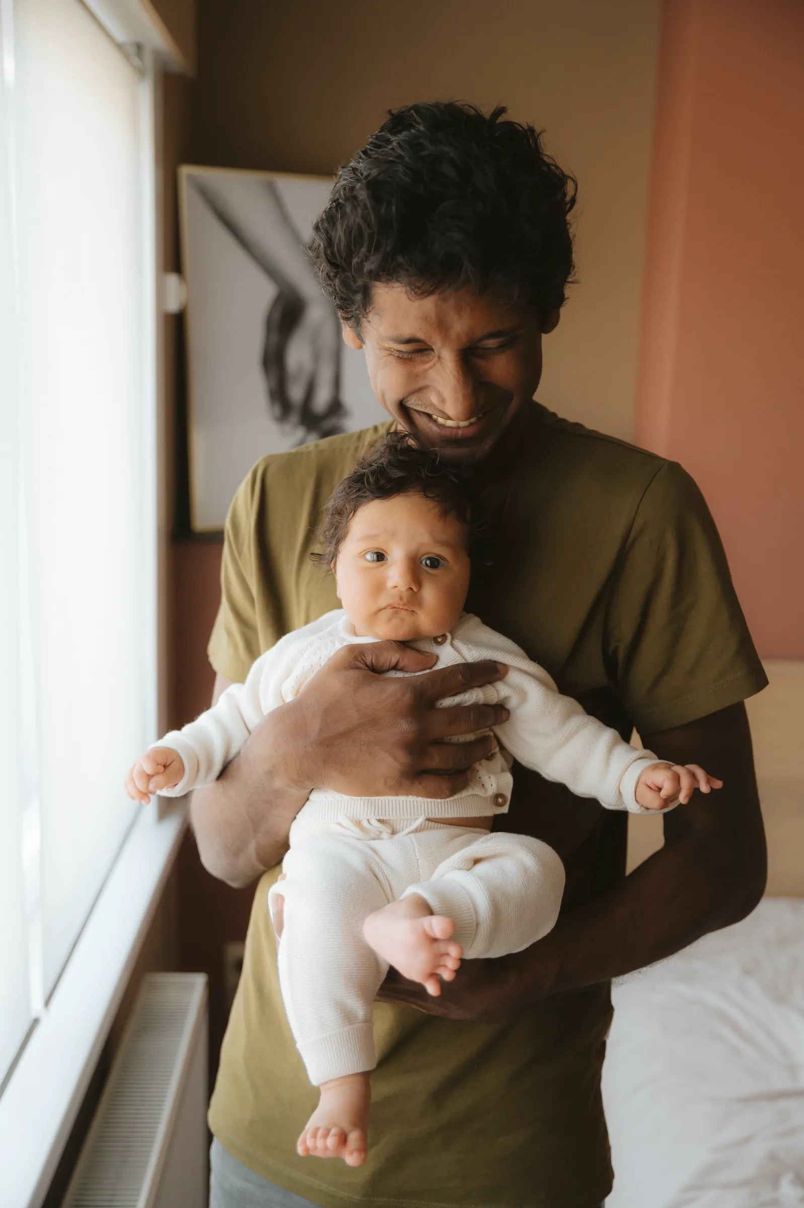 Intens genietende en lachende papa met baby op de arm.